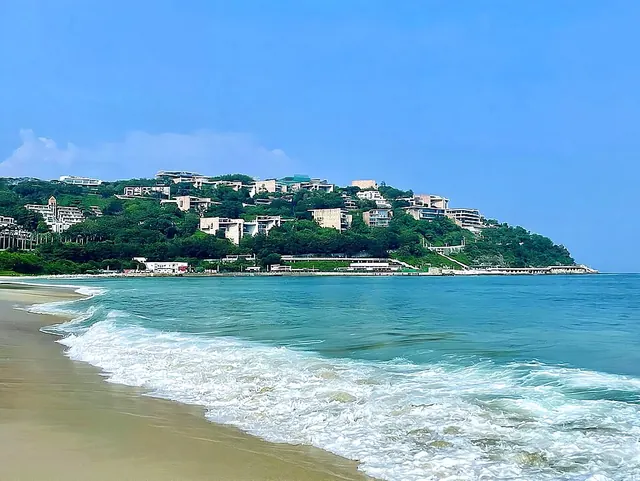 The sandy shoreline, waves and green hillside at Dameisha Beach