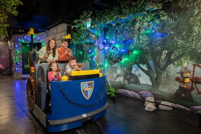 A family riding a Kingdom Quest vehicle beside illuminated themed targets