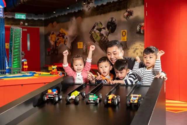 Children and an adult watching LEGO cars roll down a racing test ramp
