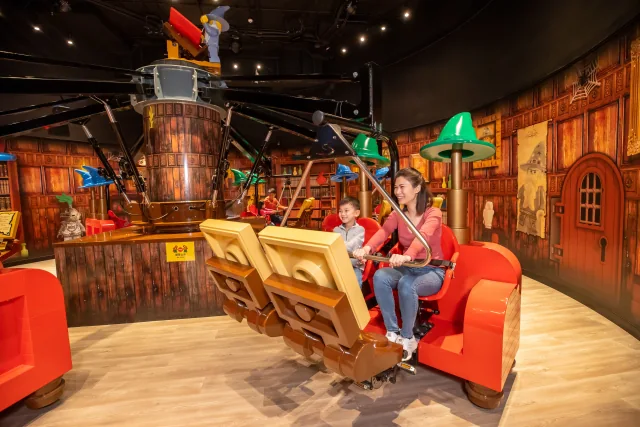 An adult and child seated on the Merlin’s Apprentice ride inside the Hong Kong attraction